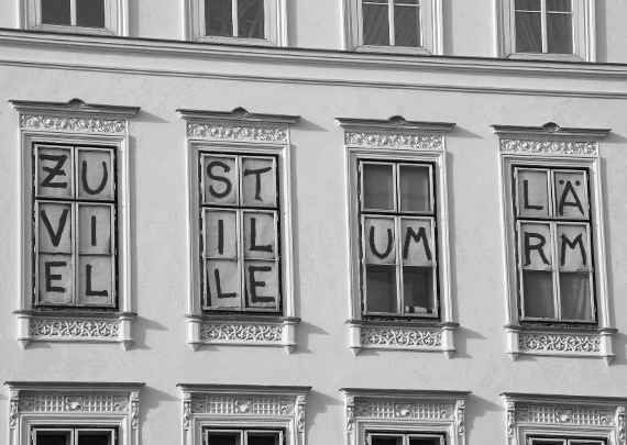 In vier Fenster eingeklebte Zettel mit Buchstaben, die den Schriftzug "Zu viel Stille um Lärm" ergeben.